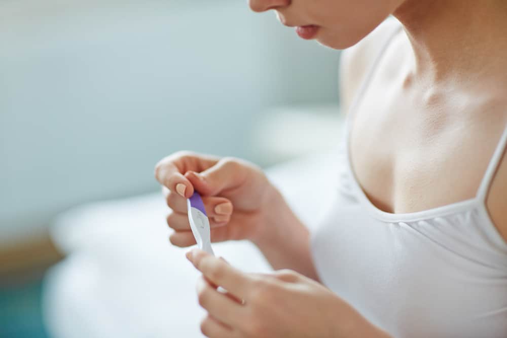 a woman looks at a pregnancy test stick in her hand