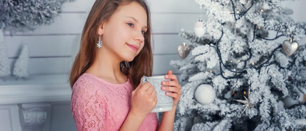 girl child near a christmas tree with a cup in hand e1619076183489