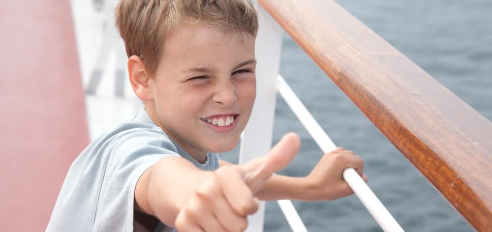 little boy shows ok on deck of big passenger ship e1619763552846