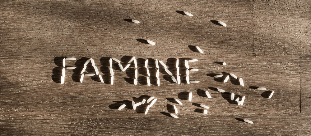 word famine made of few white rice grains on wooden table e1618121759518